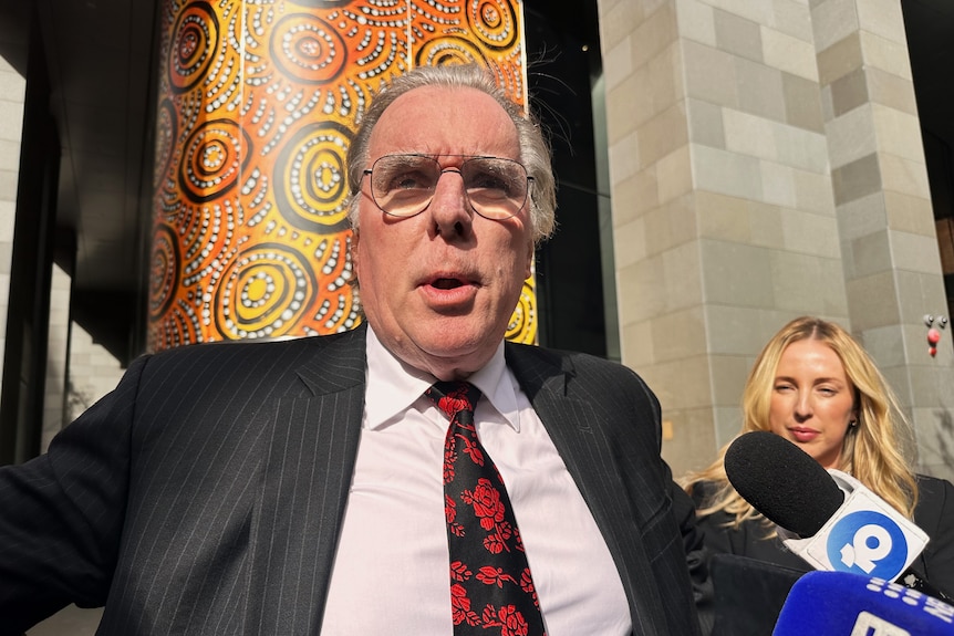 A lawyer named Martin Bennett, in a suit and tie, talks to reporters outside the courthouse. 